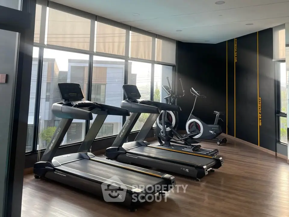 Modern gym with treadmills and exercise bikes in a bright, spacious room with large windows.