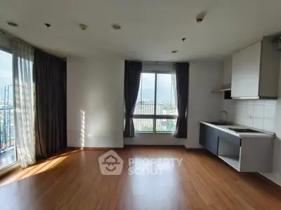 Spacious apartment with open kitchen and city view, featuring large windows and wooden flooring.