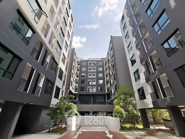 Modern apartment building exterior with lush greenery and clear blue sky.