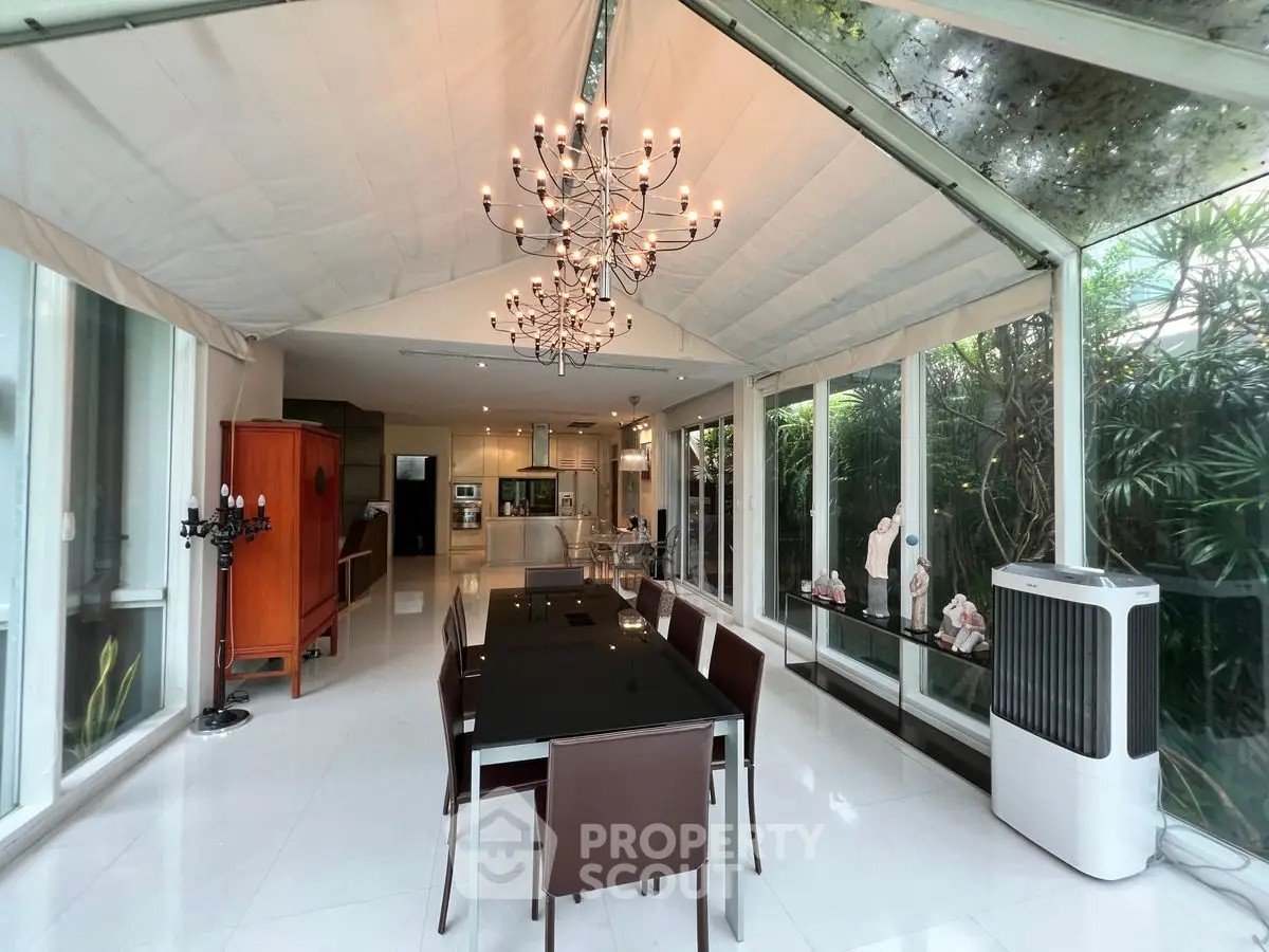 Luxurious dining area with chandelier and glass walls overlooking lush greenery
