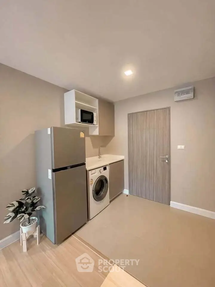 Modern compact kitchen with fridge, washing machine, and microwave in sleek apartment.