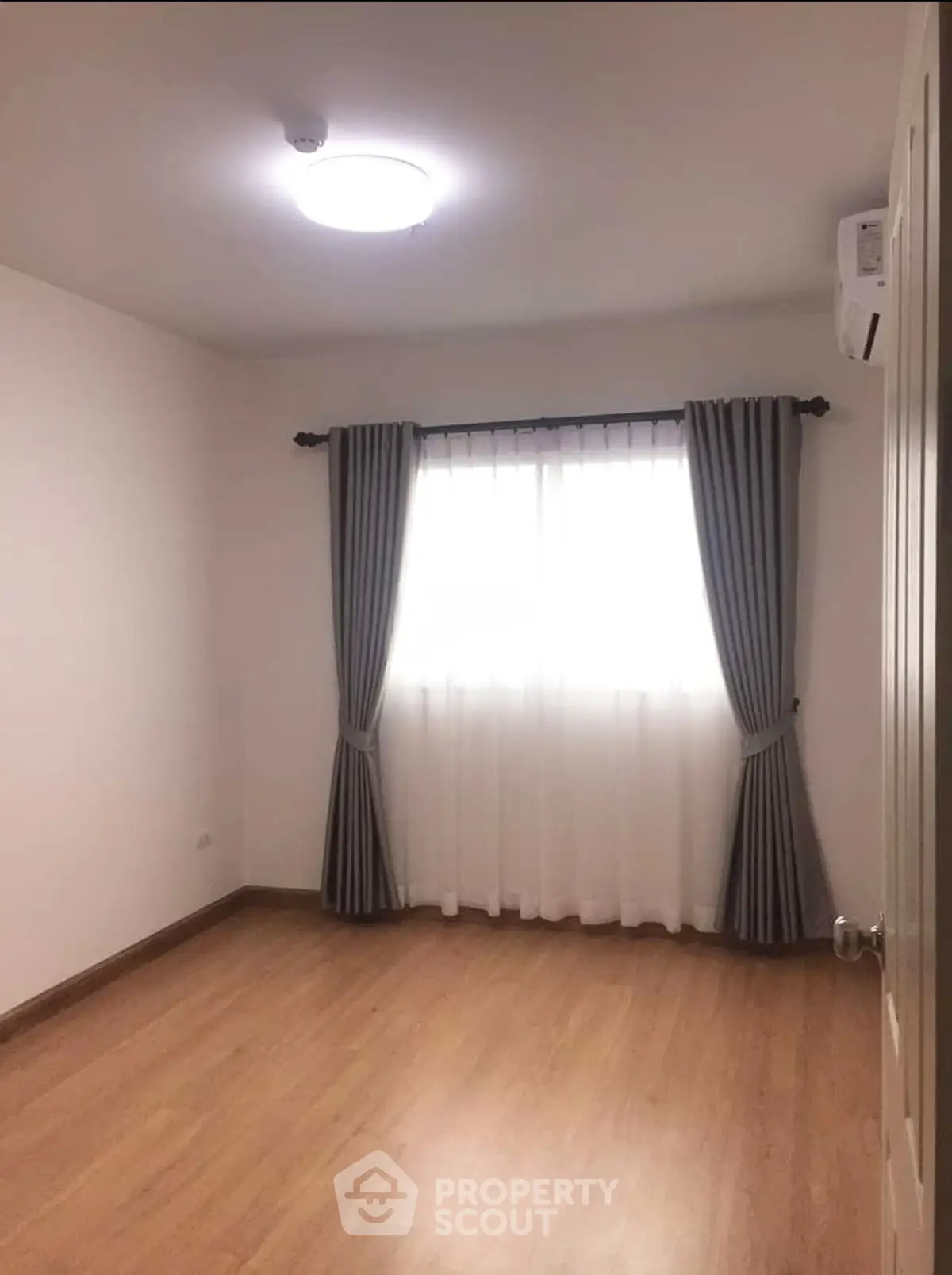 Spacious empty room with wooden flooring and elegant curtains, perfect for customization.