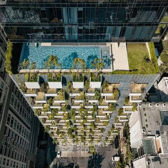 Stunning aerial view of modern building with rooftop pool and lush greenery.