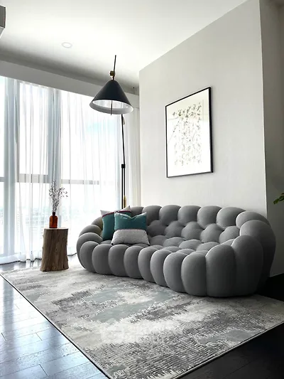 Modern living room with stylish gray sofa, floor lamp, and large window with sheer curtains.