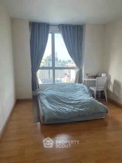 Cozy bedroom with large window and city view, featuring minimalist decor and wooden flooring.