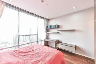 Spacious bedroom with large windows and modern furnishings in a high-rise apartment.