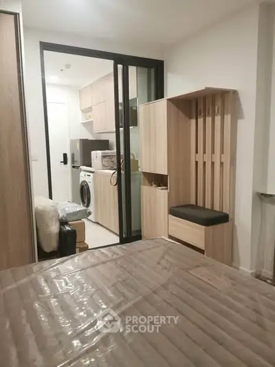 Modern studio apartment with compact kitchen and washing machine, featuring sleek wooden cabinetry and cozy seating area.