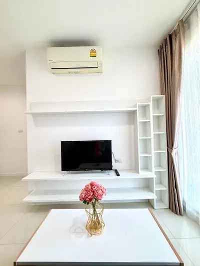Modern living room with sleek white furniture and air conditioning, featuring a stylish TV setup and elegant decor.