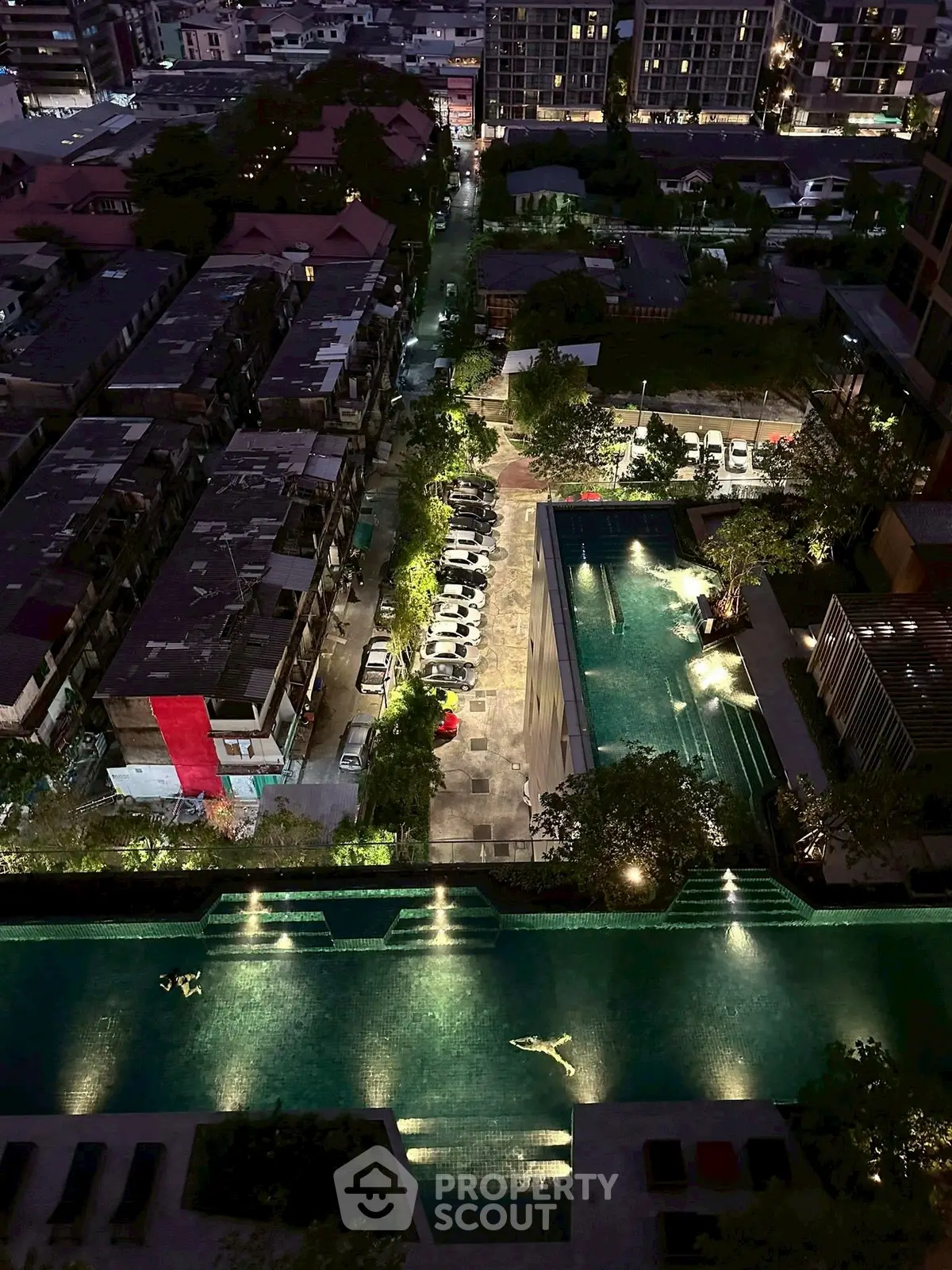 Stunning aerial view of illuminated rooftop pool and cityscape at night, showcasing luxurious urban living.