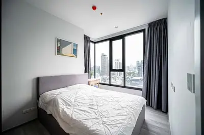 Modern bedroom with city view and large windows, featuring a cozy bed and stylish decor.