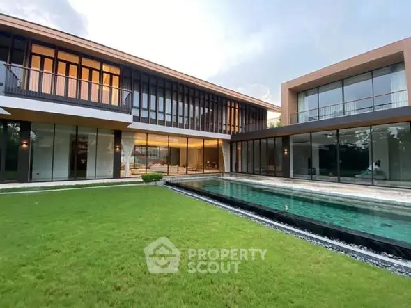 Luxurious modern home with expansive glass windows and private pool in lush green setting.