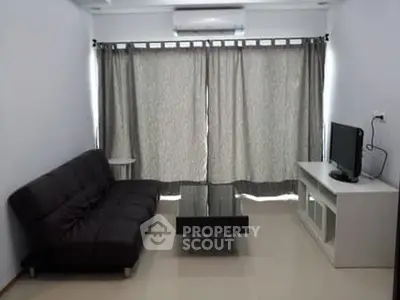 Modern living room with sleek black sofa and flat-screen TV, featuring minimalist decor and natural light.