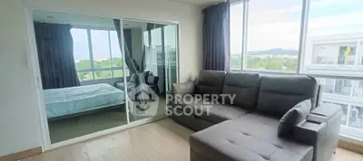 Modern living room with large windows and a view, featuring a comfortable sofa and adjacent bedroom.