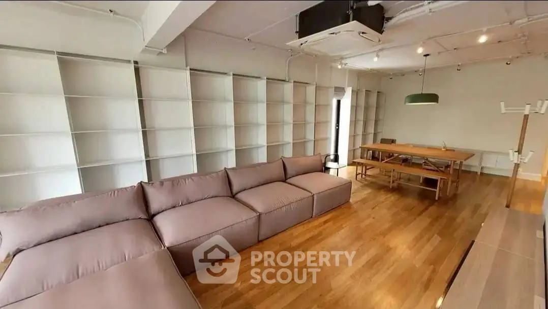 Spacious modern living room with large sofa and dining table, featuring wooden flooring and open shelving.