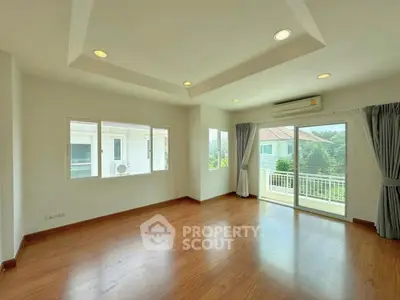 Spacious living room with wooden flooring and large windows offering natural light and balcony access.