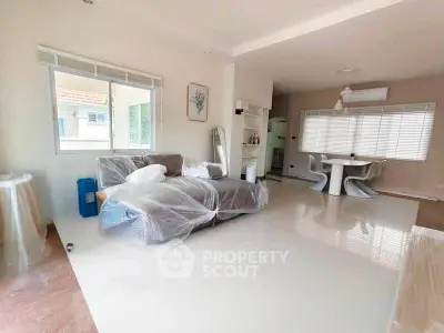 Spacious living room with modern furniture and dining area, featuring large windows and sleek flooring.