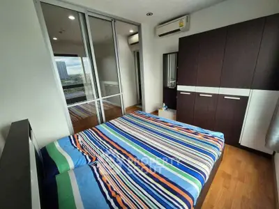 Modern bedroom with striped bedding, large wardrobe, and city view from window.