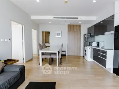 Modern open-plan living room with sleek kitchen and dining area, featuring wooden flooring and contemporary design.