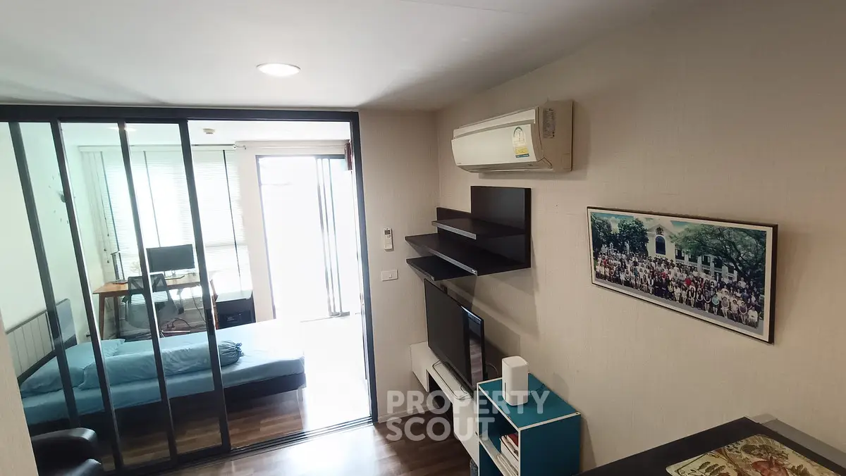 Modern apartment interior with glass partition, cozy living area, and air conditioning unit.