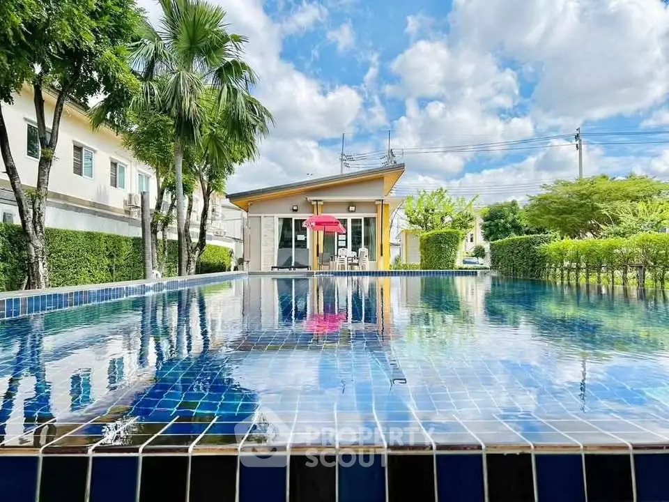 Stunning residential pool with lush greenery and modern clubhouse under a bright blue sky.