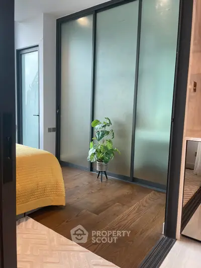 Modern bedroom with frosted glass sliding doors and wooden flooring, featuring a cozy yellow bedspread and a potted plant.
