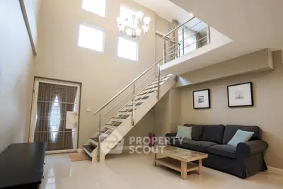 Spacious modern living room with high ceiling and mezzanine, featuring elegant staircase and cozy seating area.