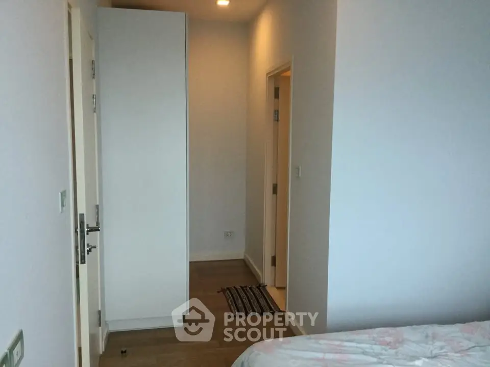 Cozy bedroom with wooden flooring and white walls, featuring a wardrobe and a glimpse of the hallway.