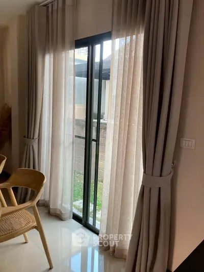 Elegant interior with floor-to-ceiling curtains and sliding glass door leading to a small garden area.