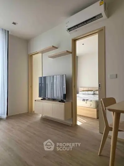 Modern living room with sleek TV setup and view into cozy bedroom, featuring minimalist decor and natural light.
