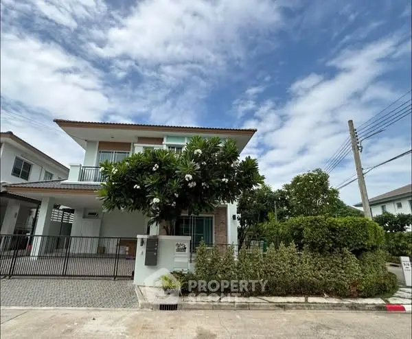 Modern two-story house with lush garden and driveway under a clear blue sky.