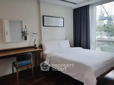 Modern bedroom with cozy bed, study desk, and city view window in urban apartment.