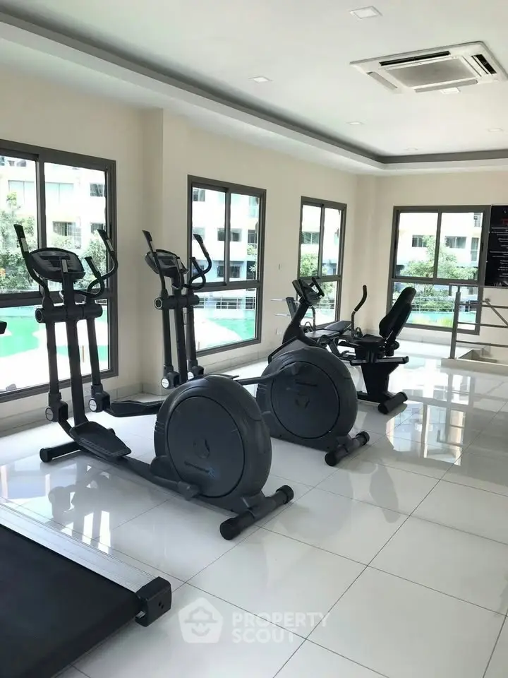 Modern gym with exercise equipment and large windows overlooking a pool area.