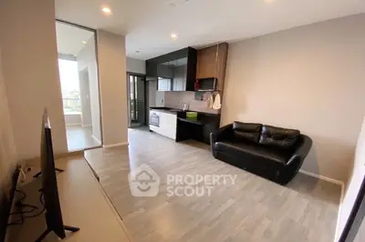 Modern living room with sleek kitchen and cozy black sofa, featuring open layout and balcony access.