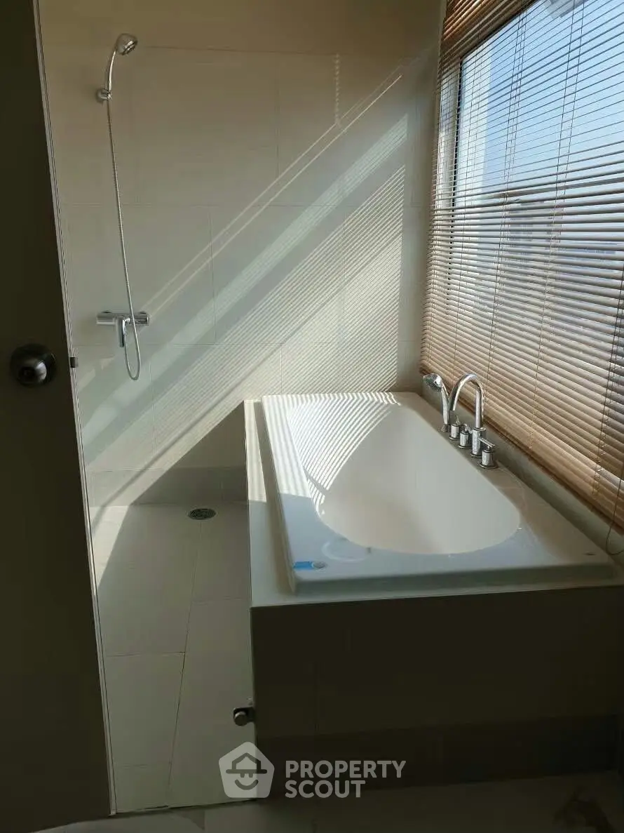 Elegant bathroom with modern bathtub and shower, featuring natural light through wooden blinds.