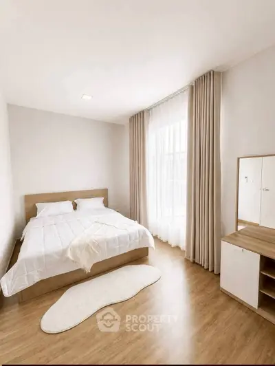 Modern bedroom with wooden flooring, cozy bed, and natural light through large window.