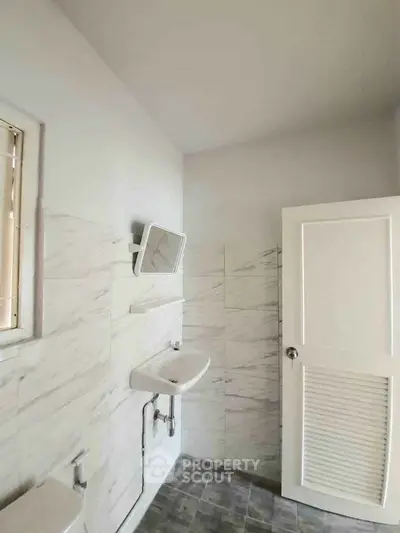Modern bathroom with sleek white fixtures and marble tile walls, featuring a compact sink and mirror.