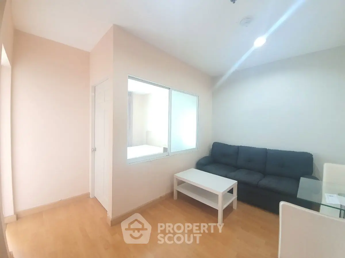 Bright living room with modern sofa and coffee table, featuring wooden flooring and ample natural light.