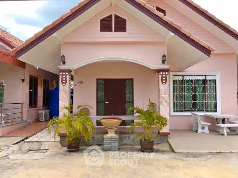 Charming single-story pink house with front porch and potted plants, perfect for cozy living.