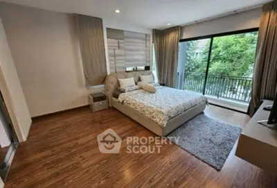 Spacious bedroom with modern decor and balcony view, featuring hardwood floors and large windows.