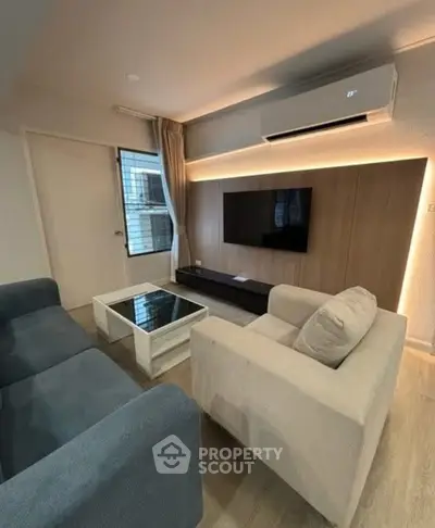 Modern living room with sleek furniture and wall-mounted TV, featuring ambient lighting and air conditioning.