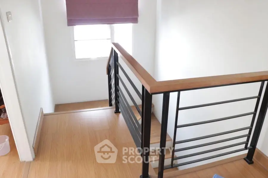 Modern staircase with wooden flooring and sleek metal railing in a bright home interior.