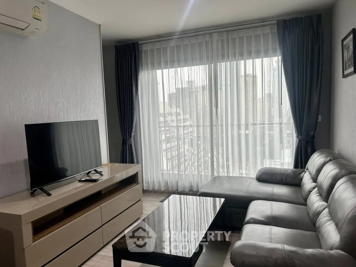 Modern living room with sleek furniture and large window offering city views.