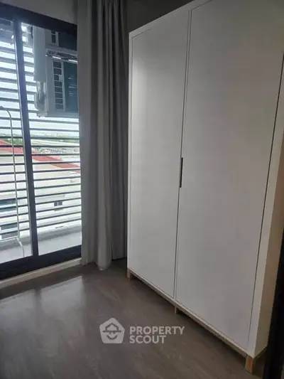 Modern bedroom with sleek wardrobe and large window offering natural light and outdoor view.