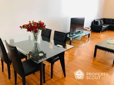 Spacious living room with gleaming hardwood floors, elegant glass dining table set, and plush black sofas, perfect for modern living.