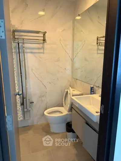 Modern bathroom with sleek fixtures and marble walls, featuring a spacious mirror and elegant design.