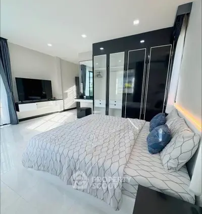 Modern bedroom with sleek black wardrobe and large TV, featuring stylish bedding and ample natural light.
