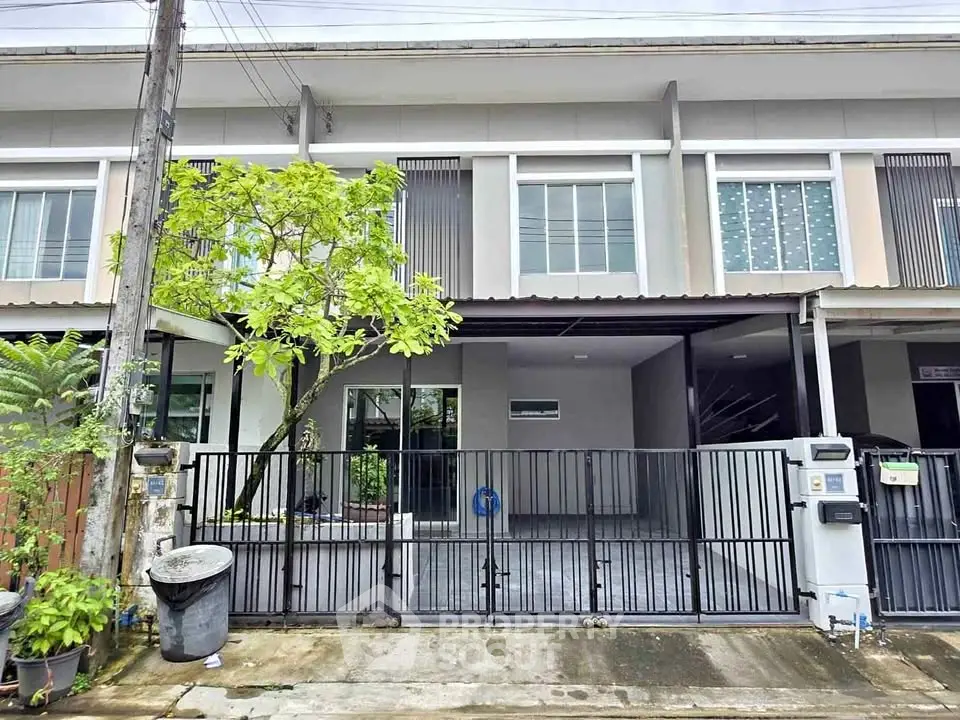 Modern townhouse exterior with gated parking and lush greenery.
