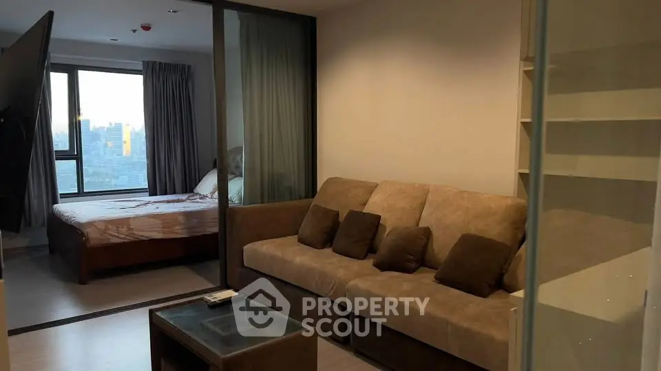 Modern apartment with cozy living room and bedroom view, featuring a comfortable sofa and cityscape window.