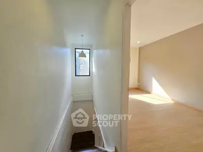 Bright hallway with wooden stairs and large window leading to spacious room