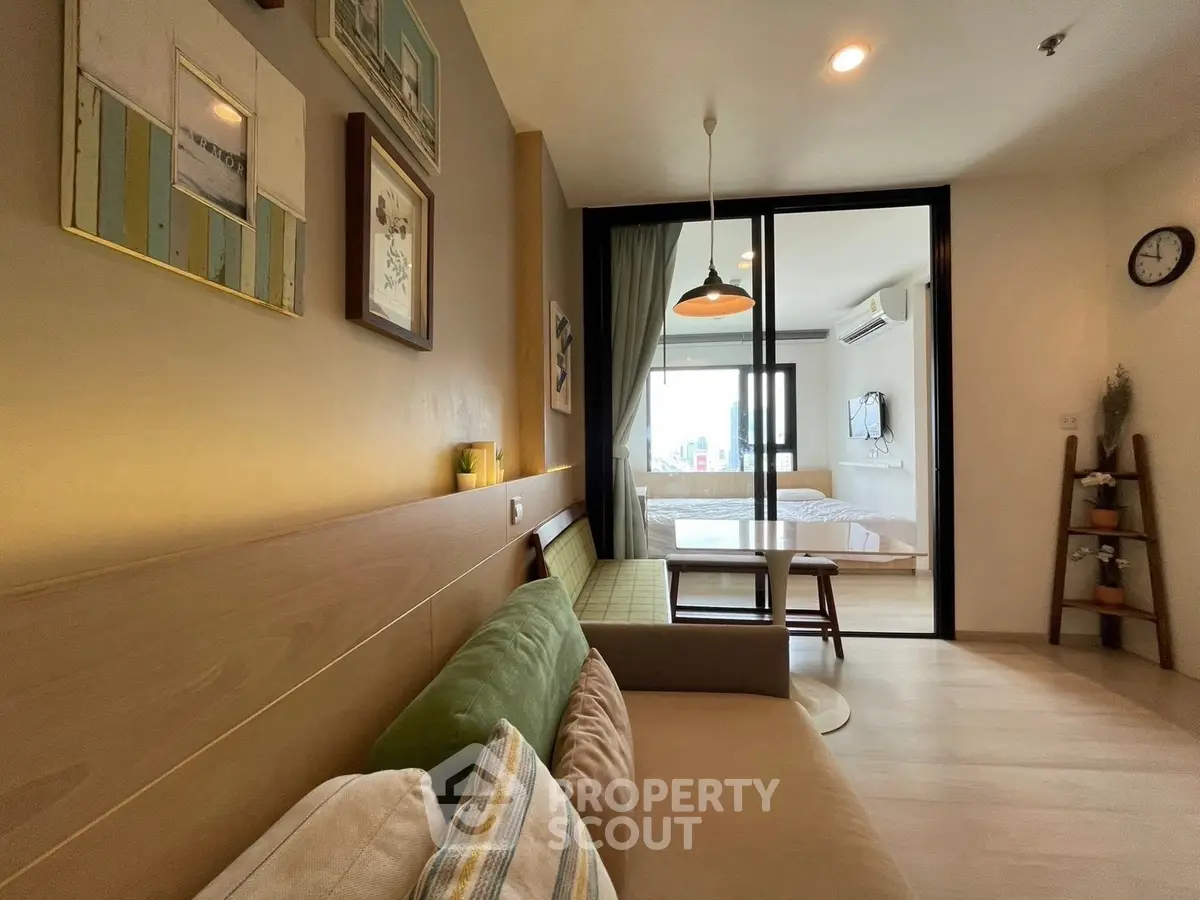 Modern living room with cozy sofa and view into stylish bedroom through glass partition.
